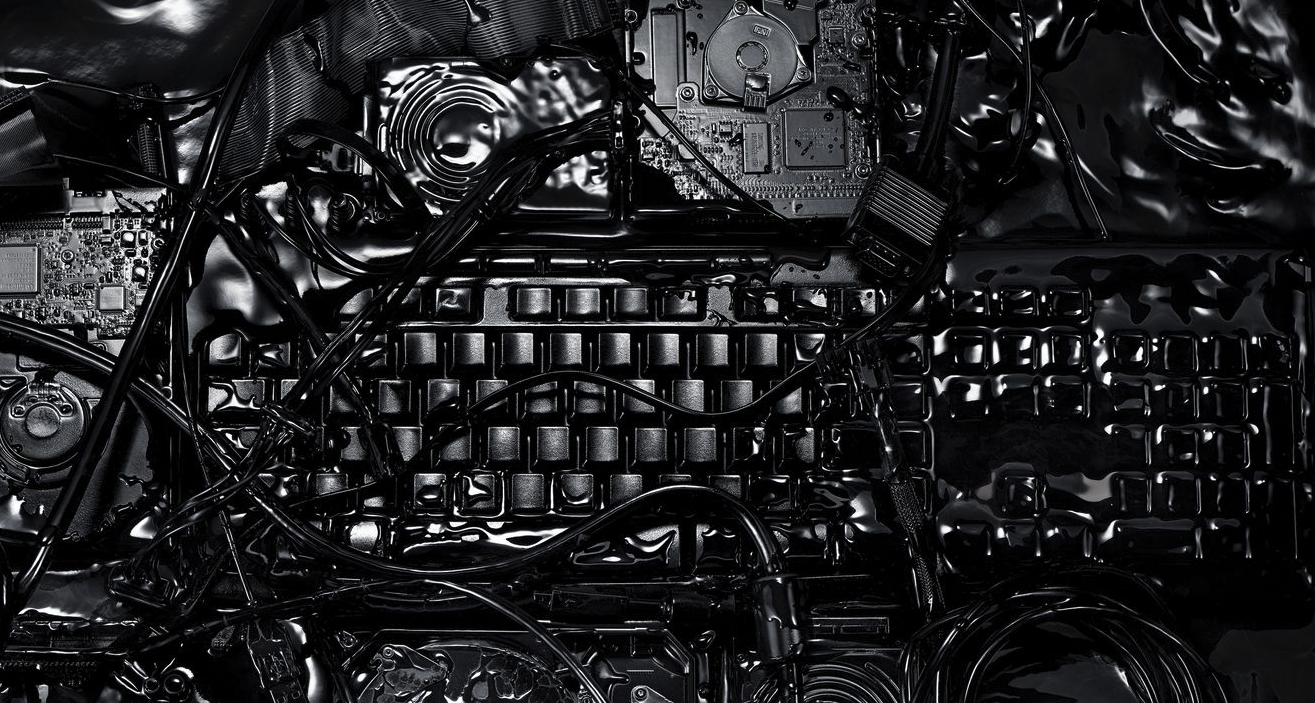 A black computer keyboard covered in other black computer devices, wires, and a black metallic liquid.